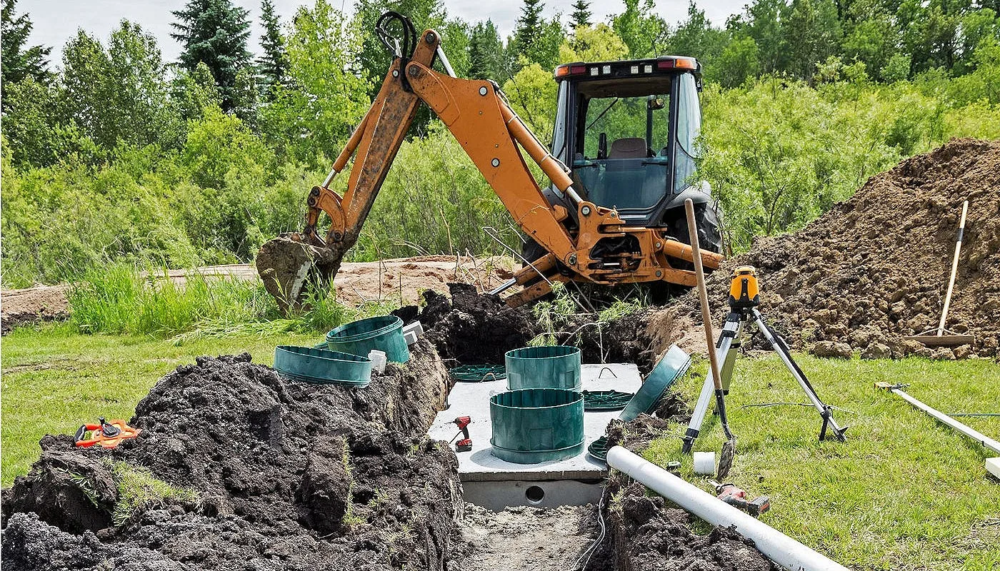Backhoe beside a new septic tank with green risers before backfill